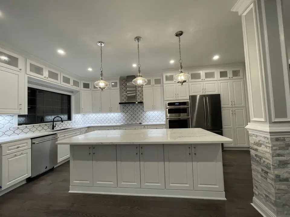 Kitchen remodeling by Kernersville company Above & Beyond: white kitchen with a large marble-look island, glass-front upper cabinets and arabesque tile backsplash