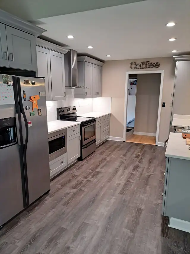 Galley side of a kitchen with gray cabinets, white countertops, stainless appliances and gray plank flooring