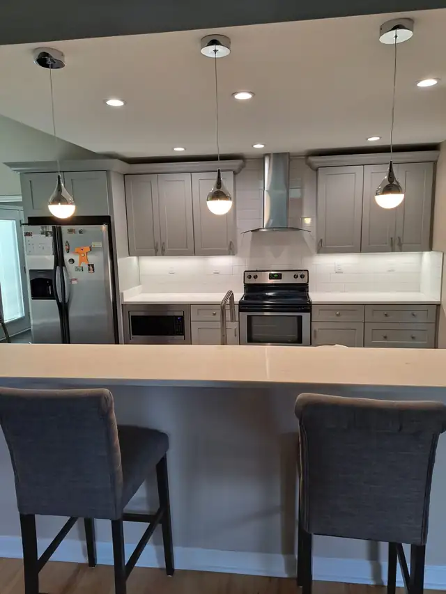 Gray shaker kitchen with a stainless range hood, three pendant lights and a white peninsula countertop