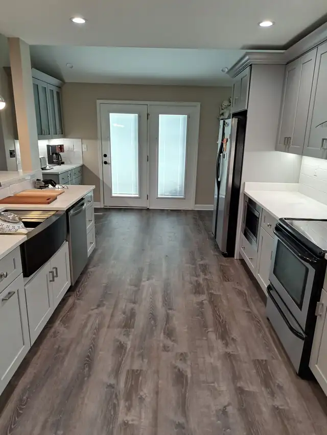 Remodeled kitchen with gray cabinets and wood-look plank flooring running through to glass patio doors